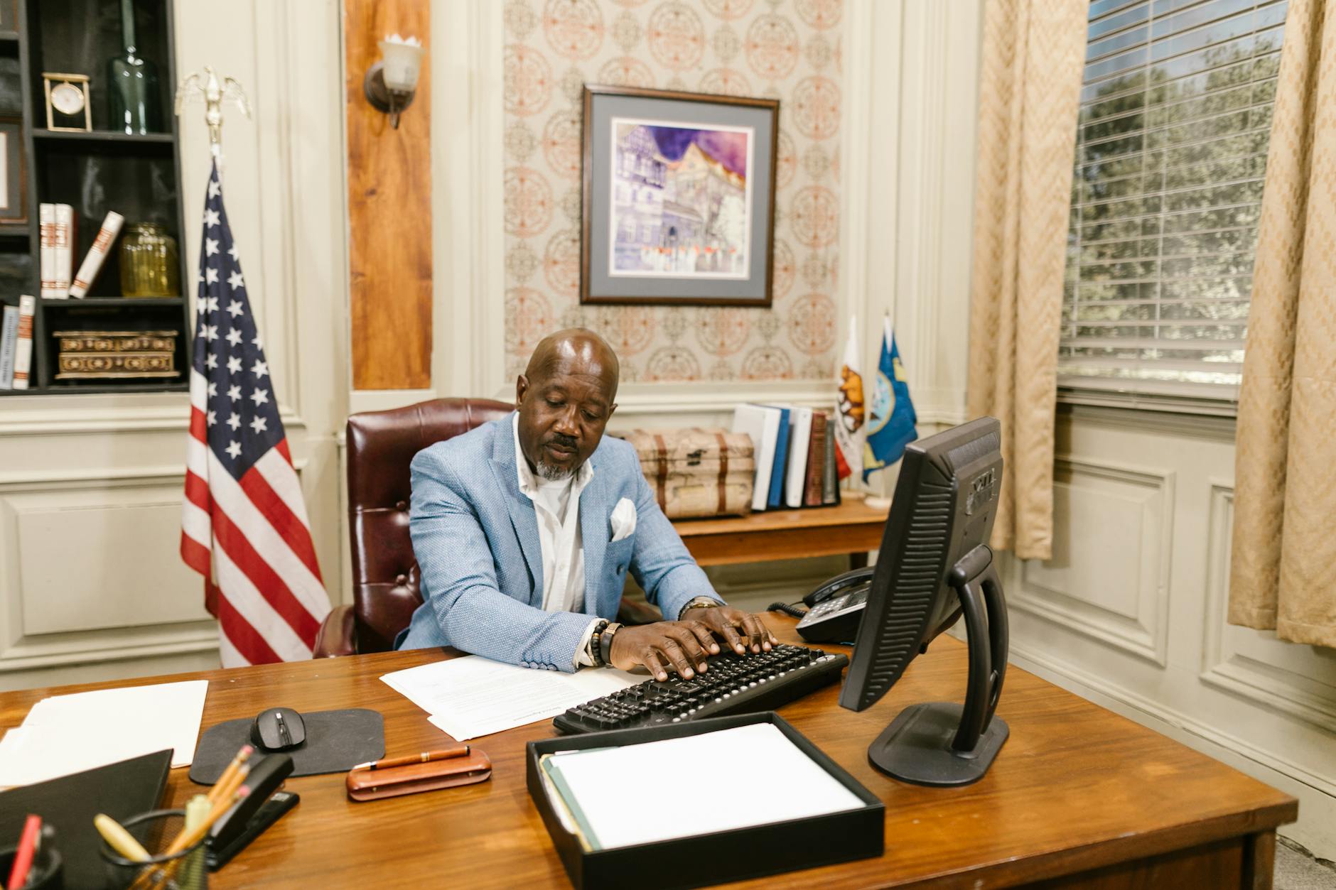 A lawyer in a suit working at his desk in an office with an American flag. — pijushsaha.com