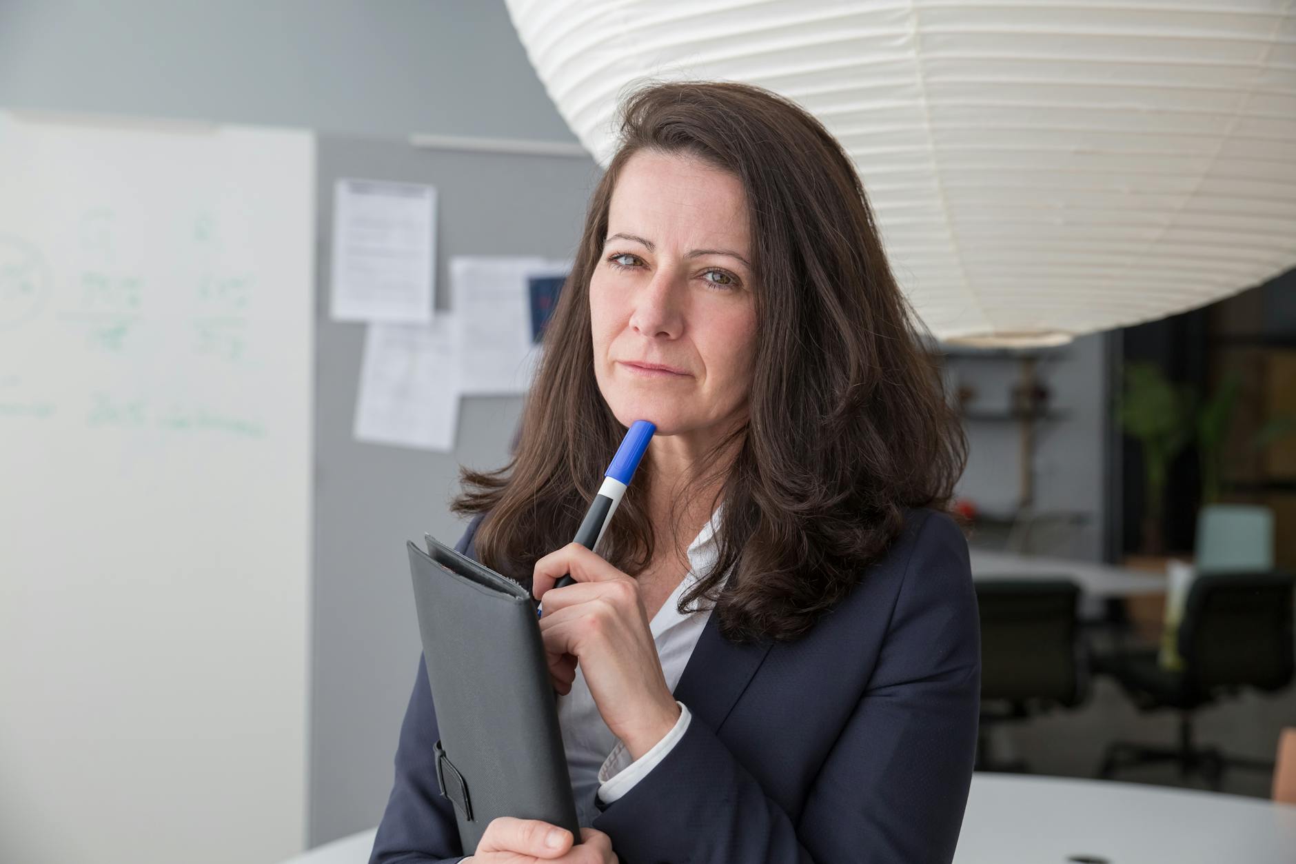 Businesswoman in corporate attire posing with a pen in a modern office setting. -- pijushsaha.com