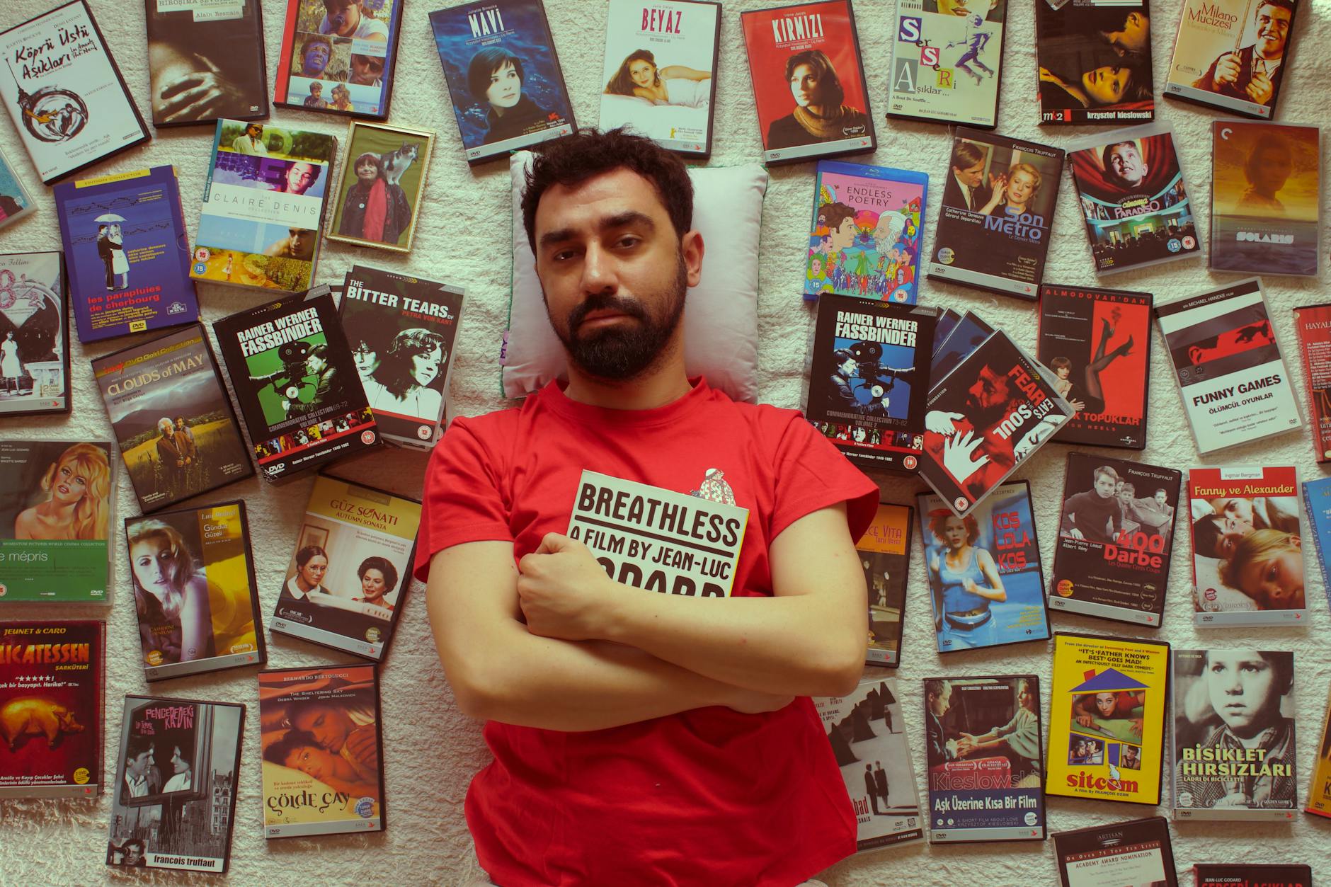 Man in red t-shirt surrounded by various DVD covers laying on a textured wall. -- pijushsaha.com