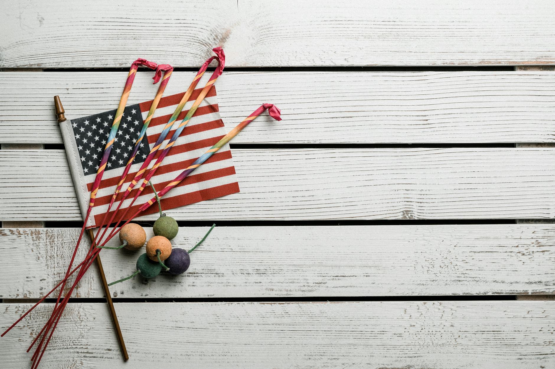 Top view of small bombs and long thin Bengal lights in vibrant multi colored wraps on Flag of United States on white wooden table -- pijushsaha.com