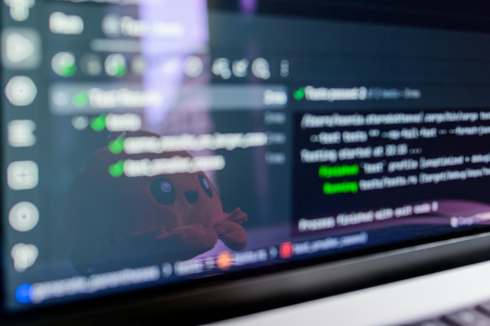 Close-up of a laptop screen displaying programming code with a cute plush toy reflecting. — pijushsaha.com