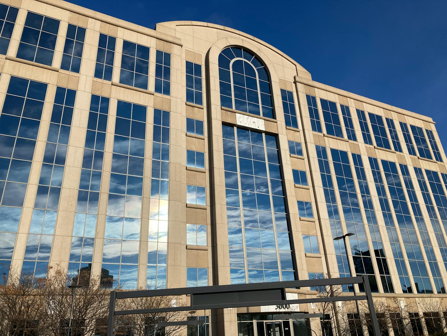 A modern office building with a striking glass facade reflecting a blue sky. — pijushsaha.com