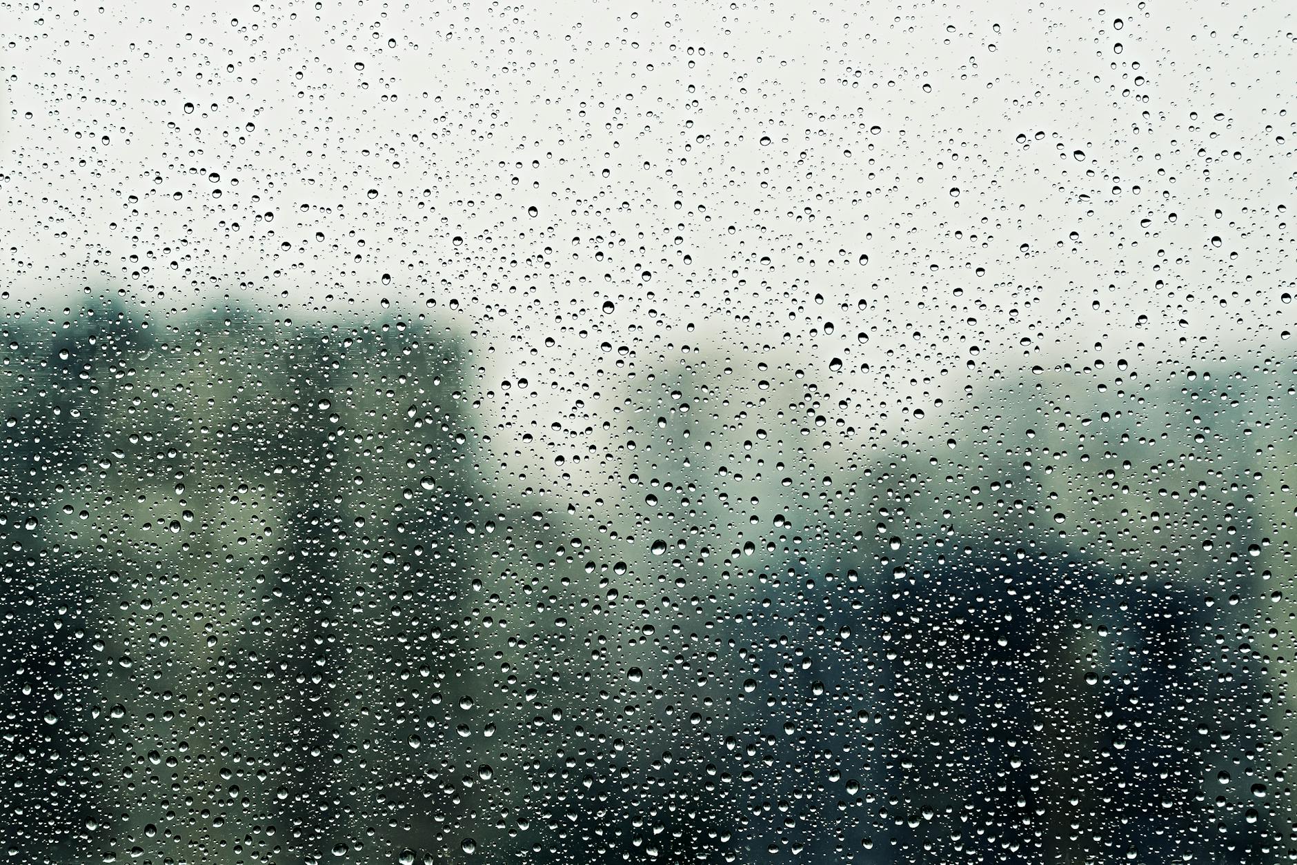 Close-up of raindrops on a window with blurred background, conveying a moody, cozy vibe. -- pijushsaha.com