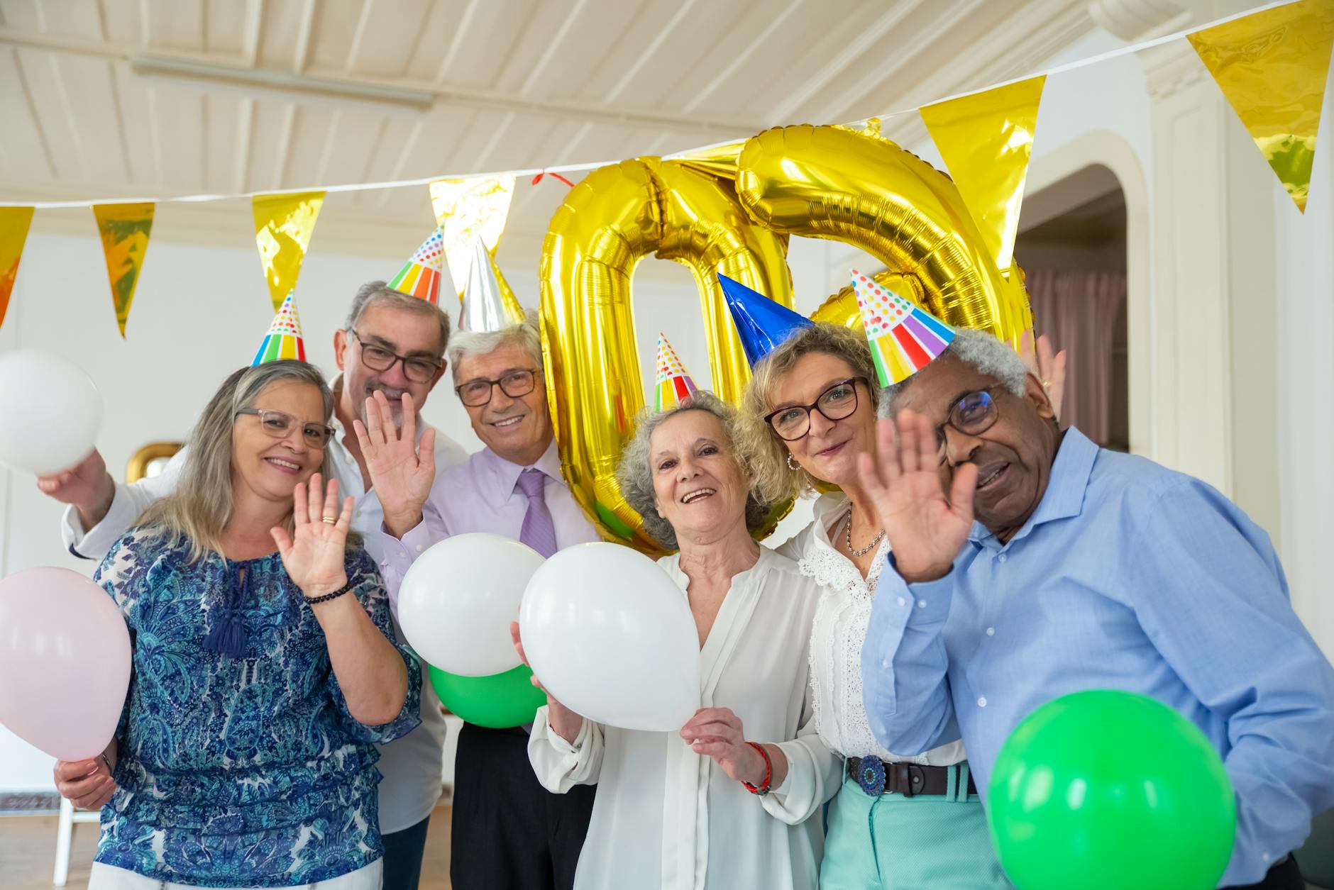 Joyful elderly group celebrating a birthday with balloons and party hats indoors. -- pijushsaha.com