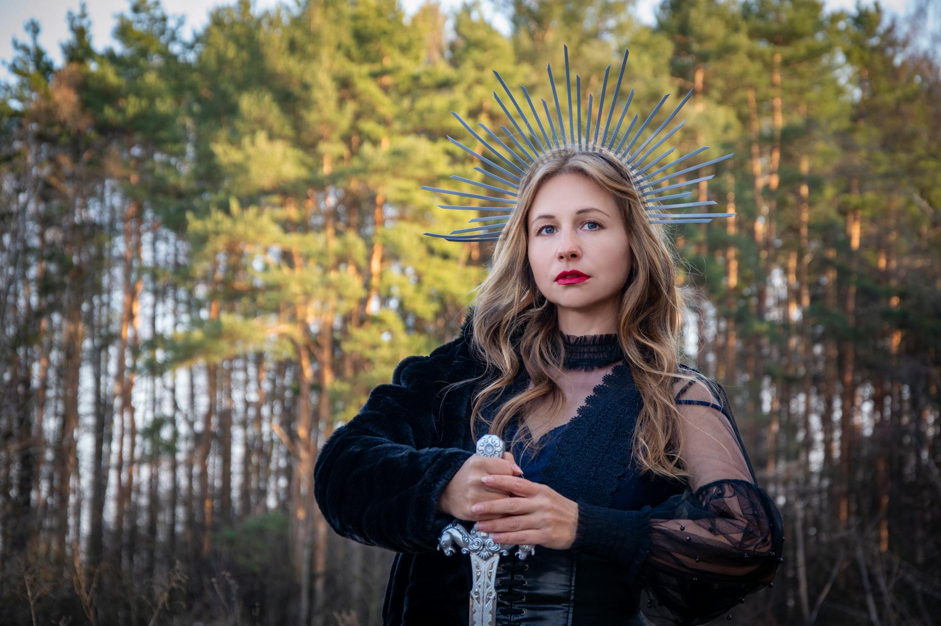A woman in black attire with a metal crown holding a sword in a forest setting. -- pijushsaha.com