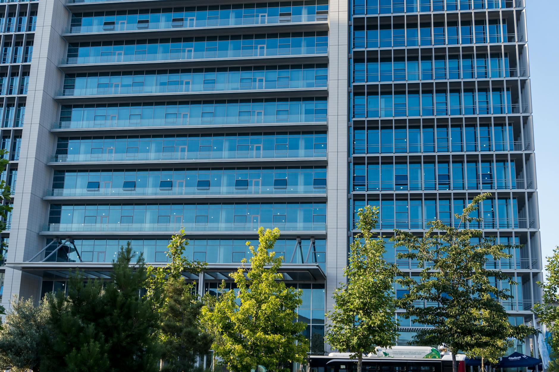 Glass facade skyscraper with trees in downtown urban scene, perfect for business and architecture themes. — pijushsaha.com