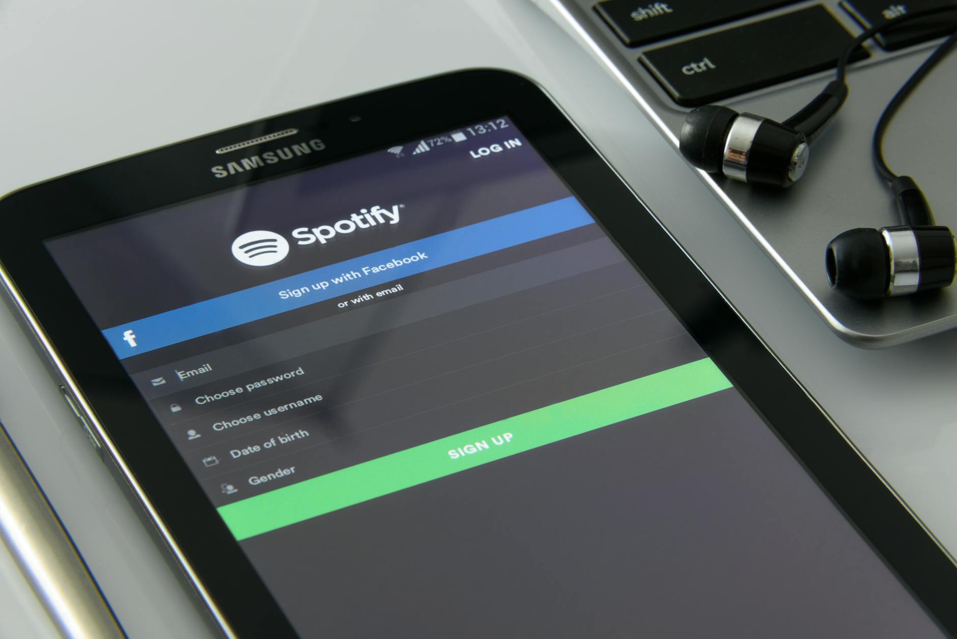 Smartphone showcasing Spotify login screen beside laptop and earphones on desk. — pijushsaha.com