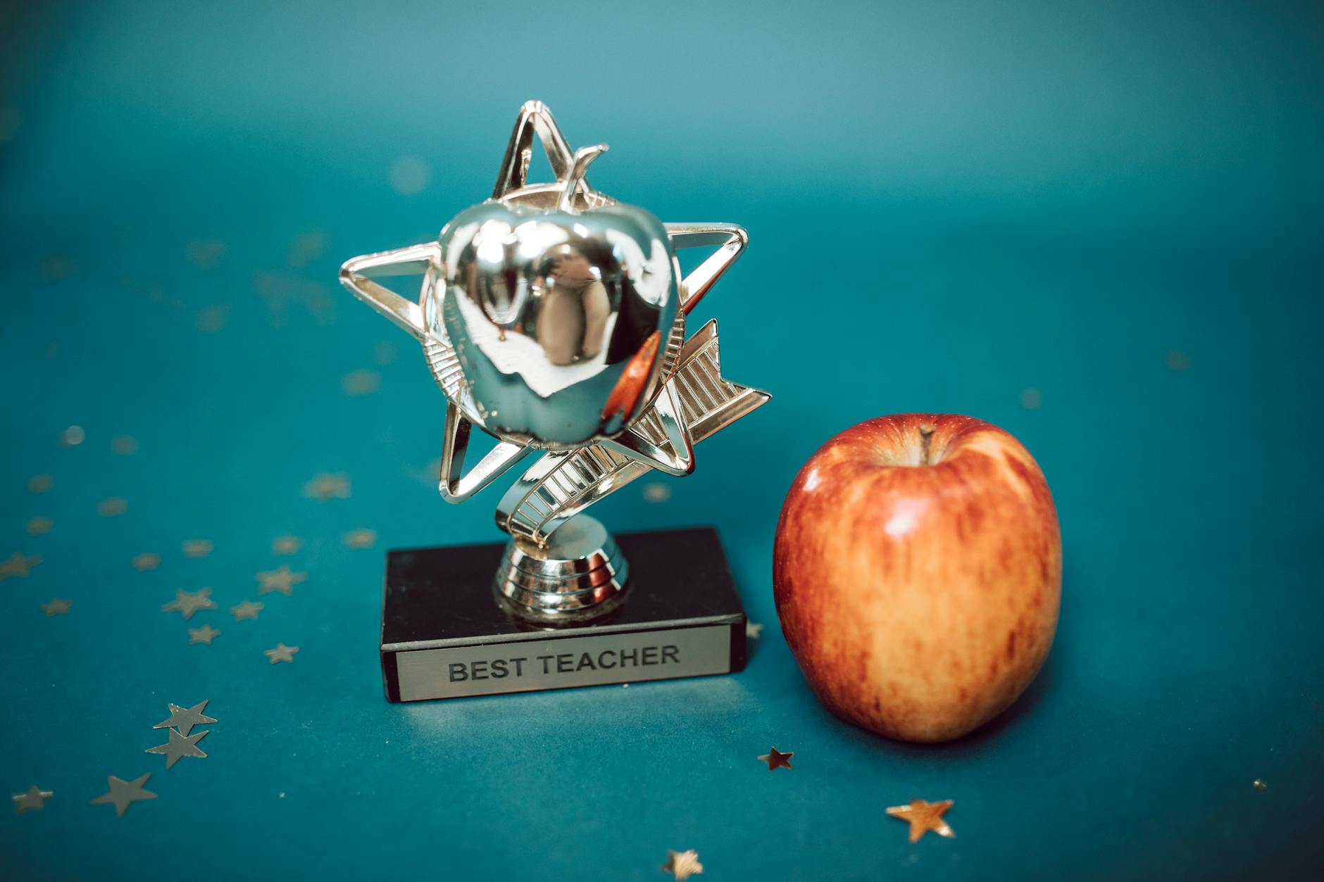 Silver star-shaped trophy with apple on a blue background for teacher appreciation. -- pijushsaha.com