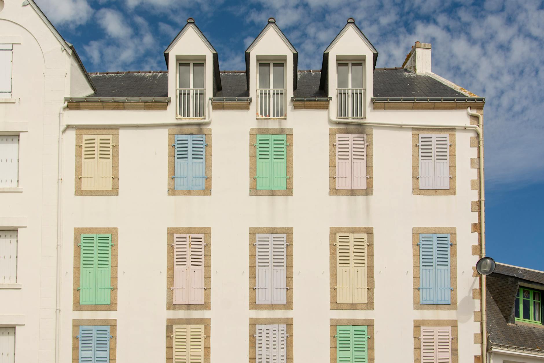 Bright pastel shutters adorn a building facade in Quiberon, capturing a serene summer day. -- pijushsaha.com