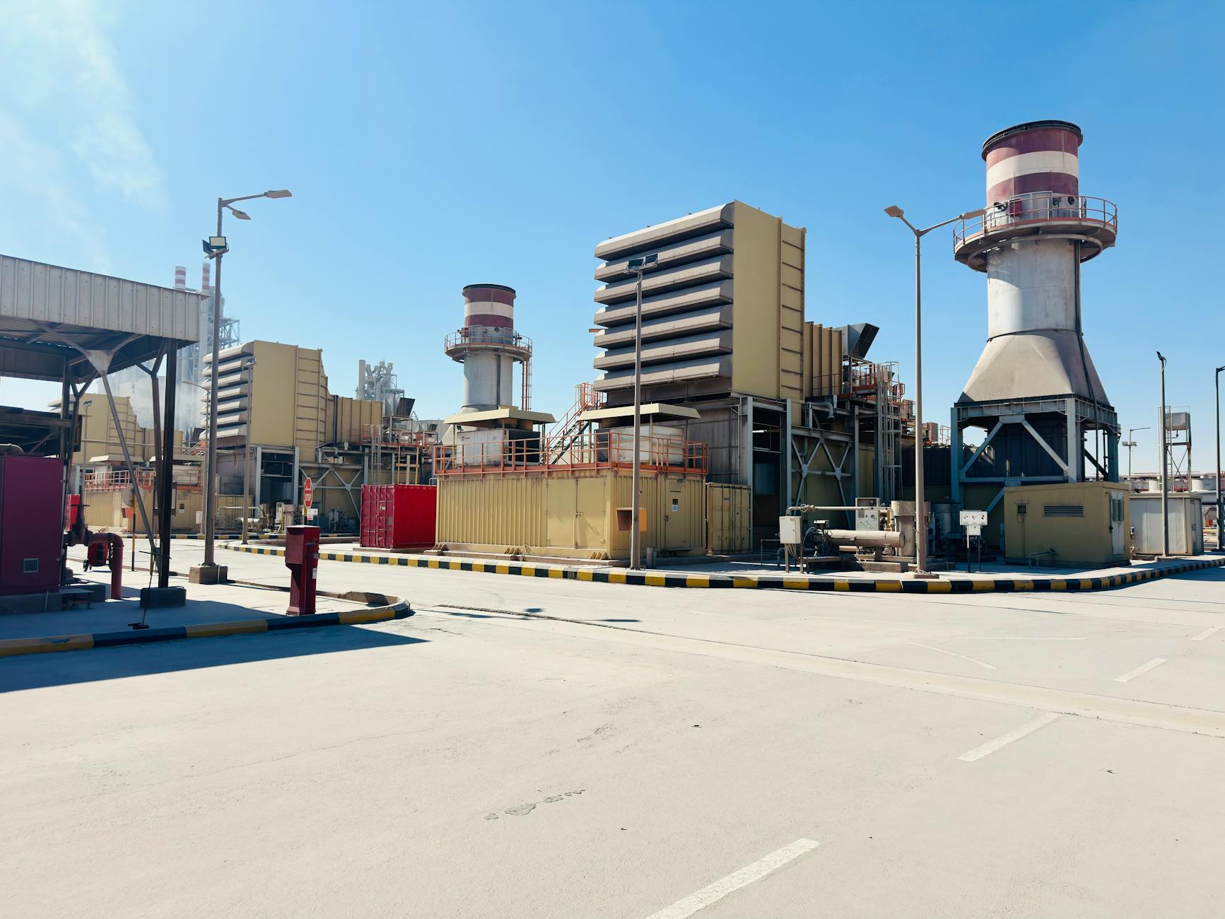 A modern power plant with turbines and chimneys under a clear blue sky in Saudi Arabia. — pijushsaha.com